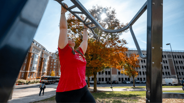woman wearing a red UMD shirt about to do a pull up